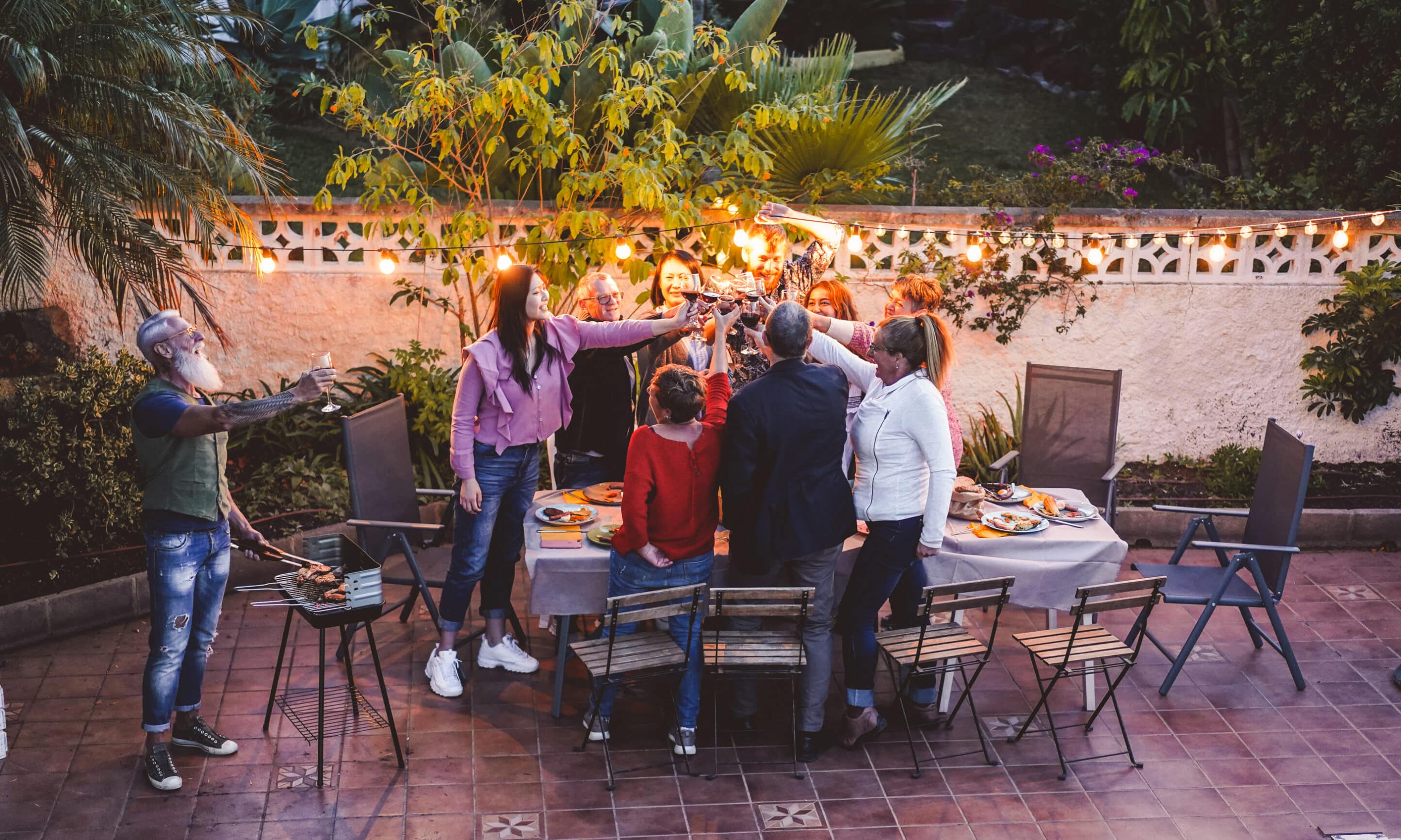 Happy friends eating and cheering with red wine at barbecue party dinner - Different age of people having fun at bbq meal sitting in villa backyard - Summer lifestyle and food concept - Focus on hands